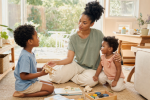 Black mother sitting calmly at eye level with her two young children in a bright family living room