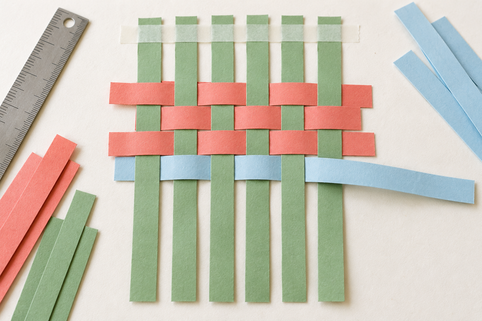 Sage paper strips interlaced with coral rows and a partially woven blue strip.